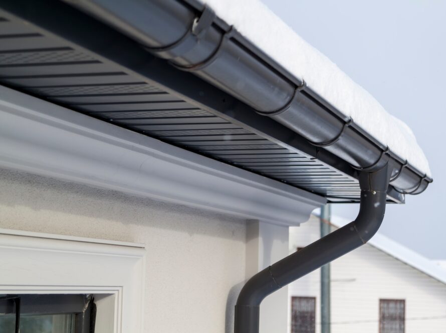 Corner of the house with new gray metal tile roof and rain gutte