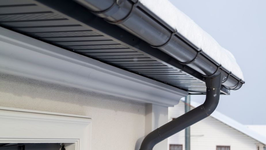 Corner of the house with new gray metal tile roof and rain gutte