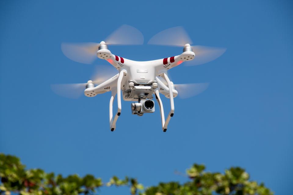 Camera drone flying in a clear blue sky above treetops