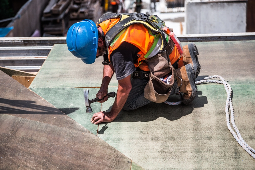 Roofer in a hard hat, safety vest and harness nailing roof sheathing