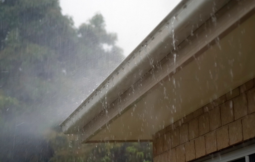 Heavy rain pouring over the gutter and roof edge of a house during a storm